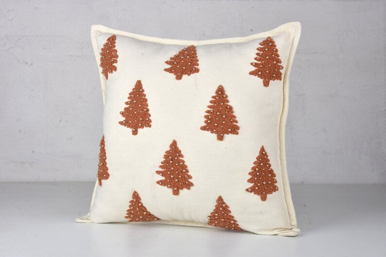 White throw pillow with brown embroidered Christmas trees and small white beads