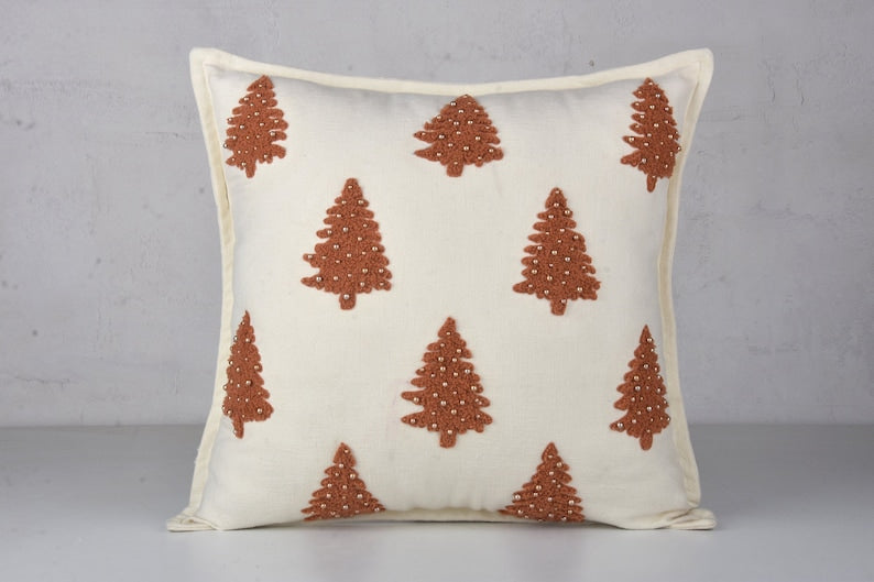 White throw pillow with brown embroidered Christmas trees and small white beads