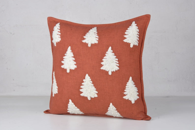 Rust-colored throw pillow with white embroidered Christmas tree design
