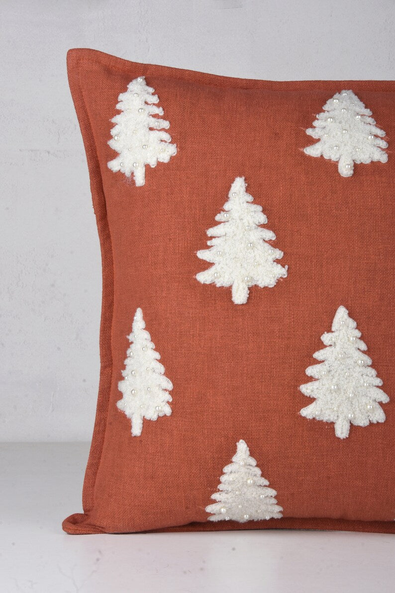 Rust-colored throw pillow with white embroidered Christmas trees and pearl-like beads