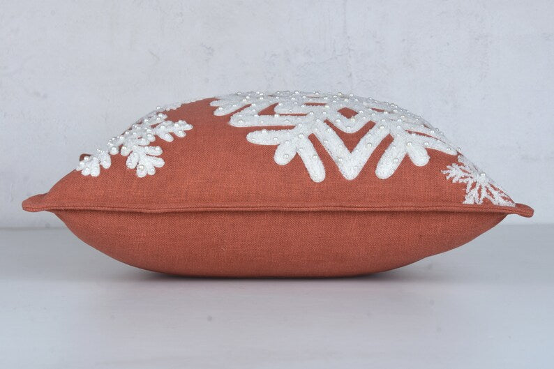 Rust-colored throw pillow with white embroidered snowflakes and beads