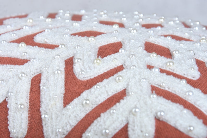 Close-up of terracotta pillow with geometric snowflake pattern and pearl embellishments