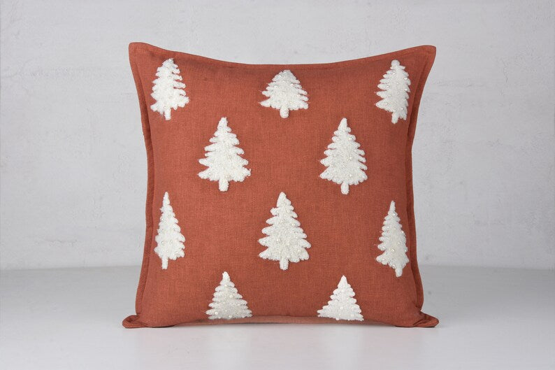 Rust-colored throw pillow with white embroidered Christmas tree pattern